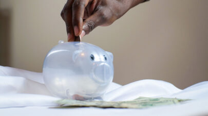 Zoomed in photo of hand putting money into a plastic piggy bank.